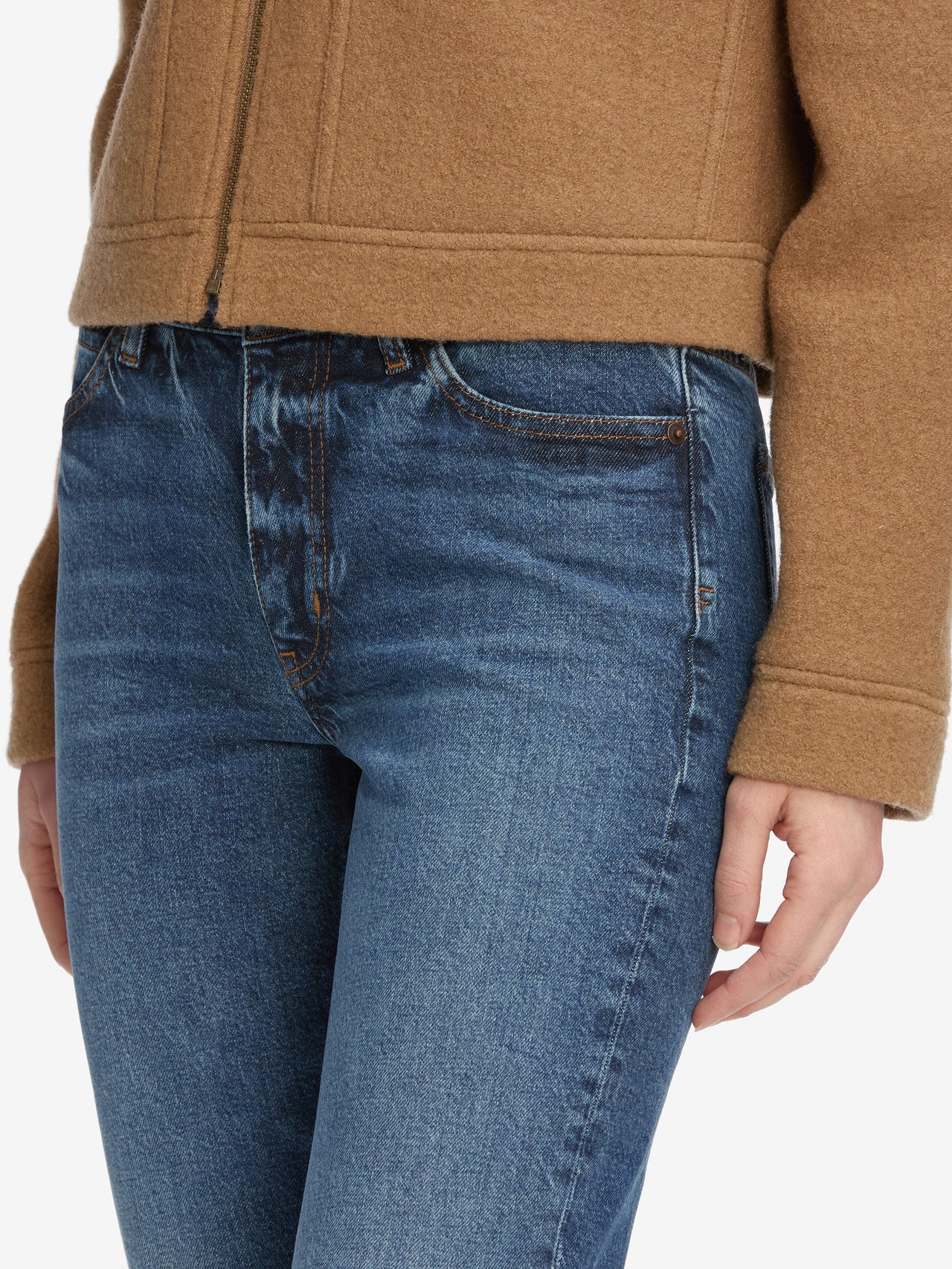 Person wearing blue jeans and a brown jacket on a white background
