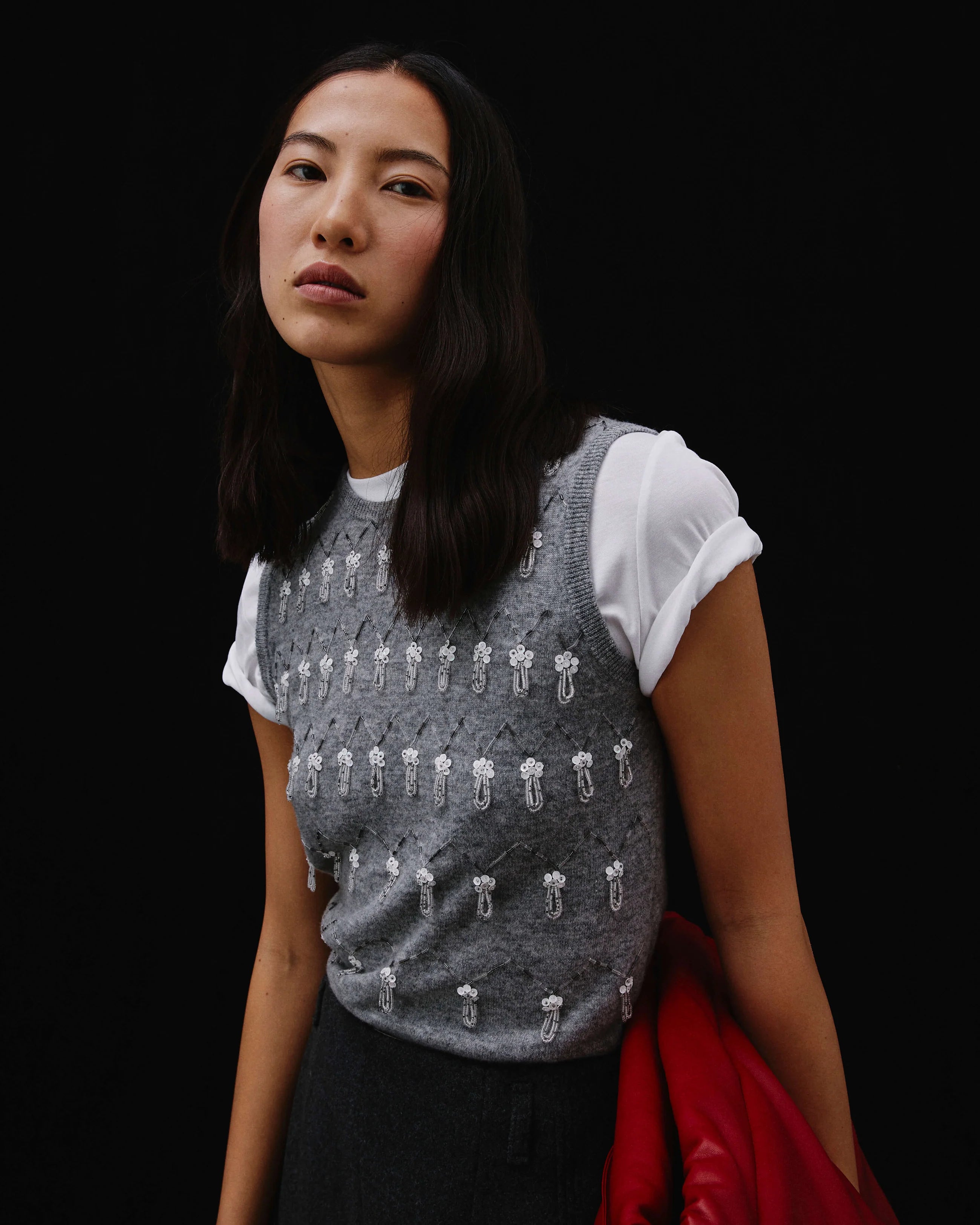 A woman wearing a gray knit vest with hand embroidery, paired with a white top and a red jacket.