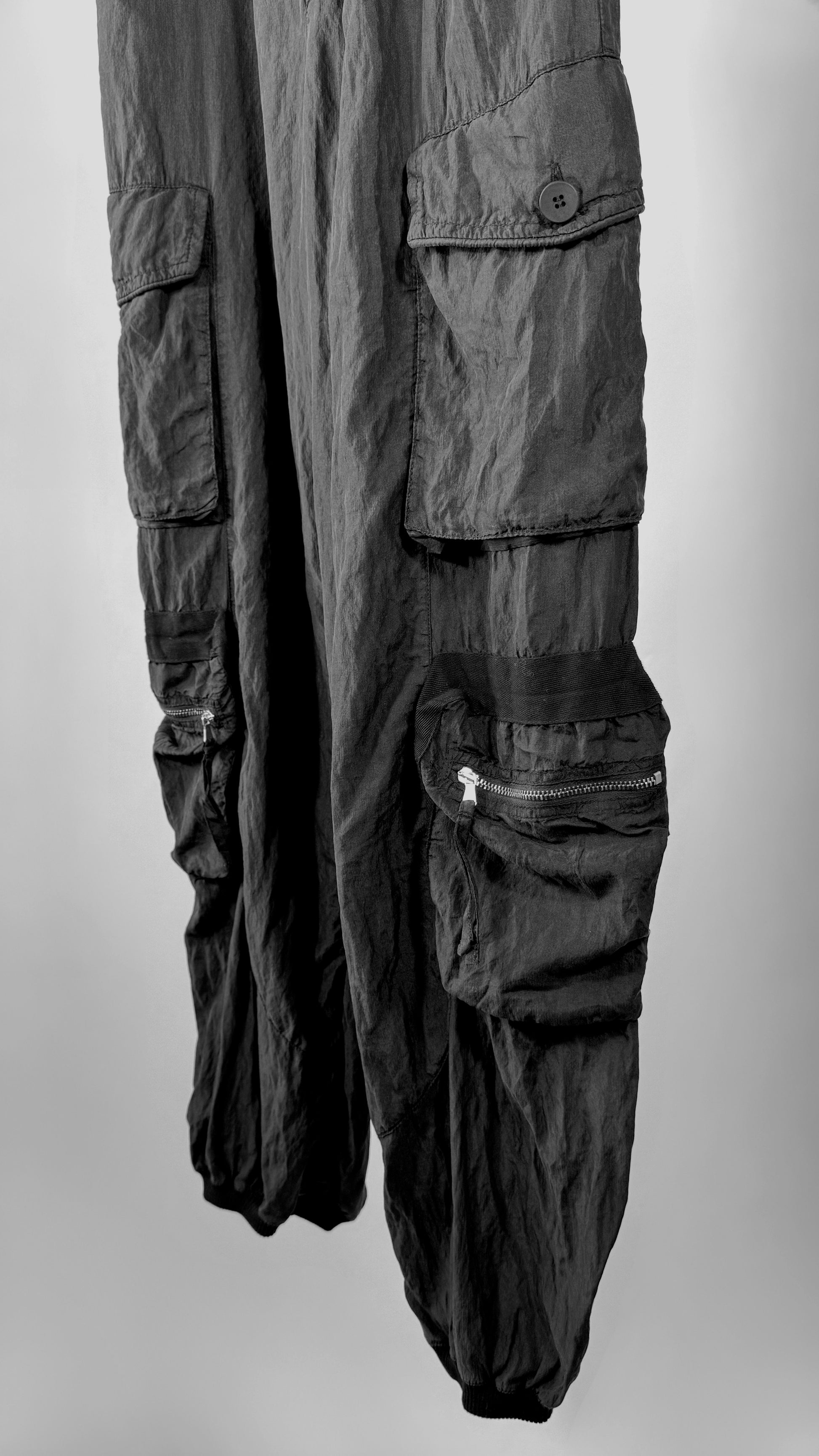 Black cargo pants with multiple pockets on a light gray background