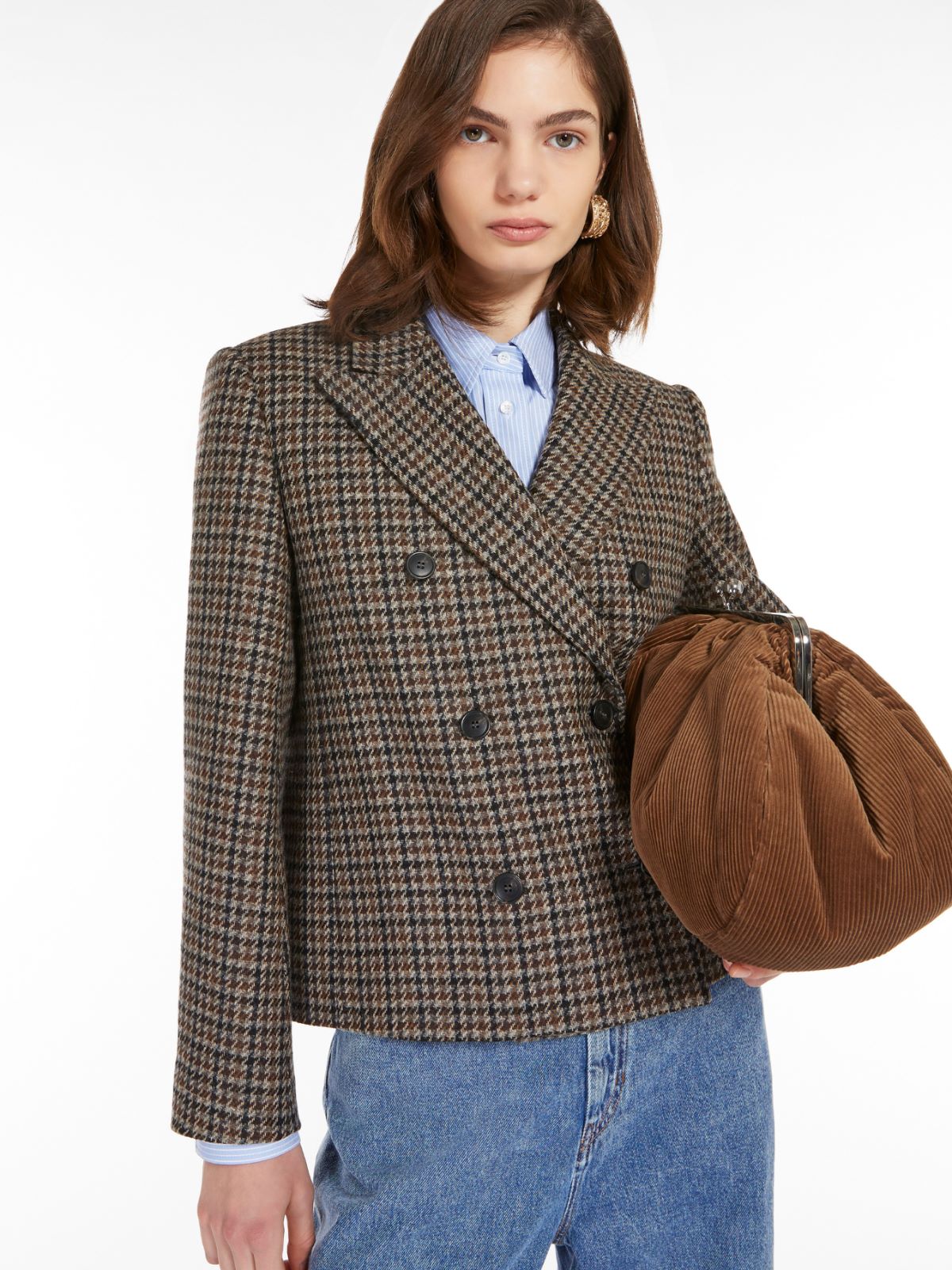 A woman wearing a houndstooth wool double-breasted blazer with a lapel collar and decorative buttons on sleeve cuffs paired with blue jeans.