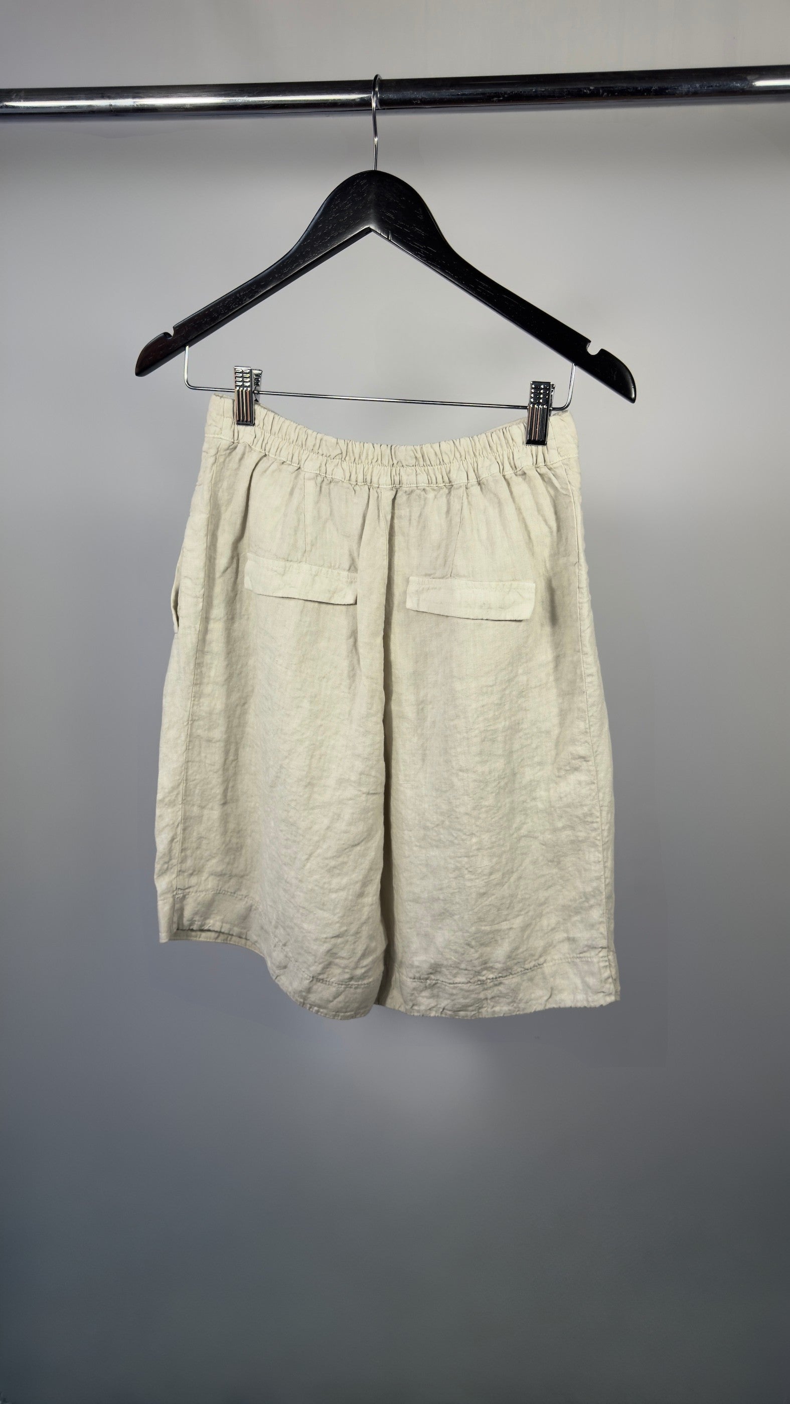 Beige shorts hanging on a black hanger against a gray background