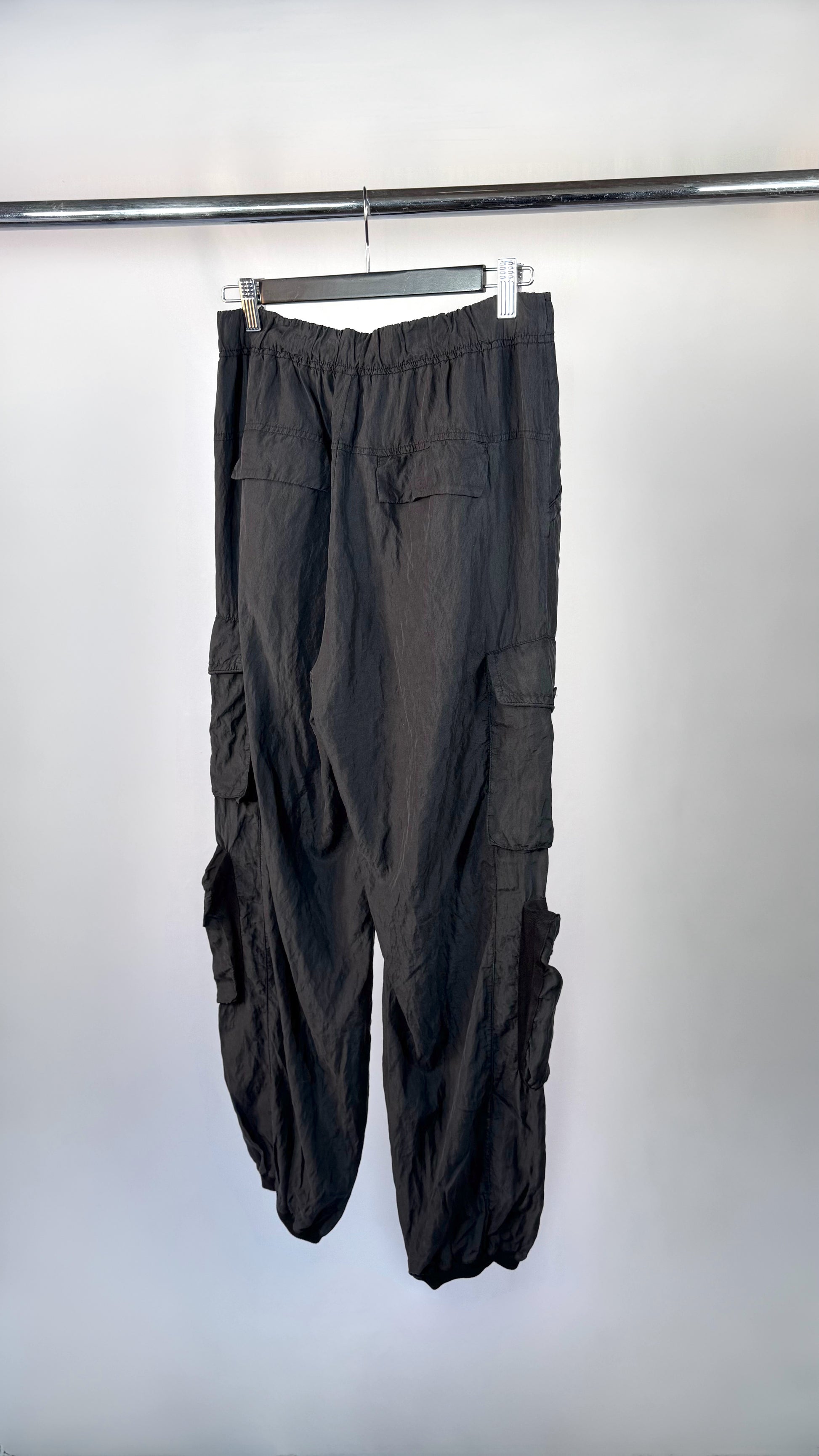 Black cargo pants hanging on a rack against a white background