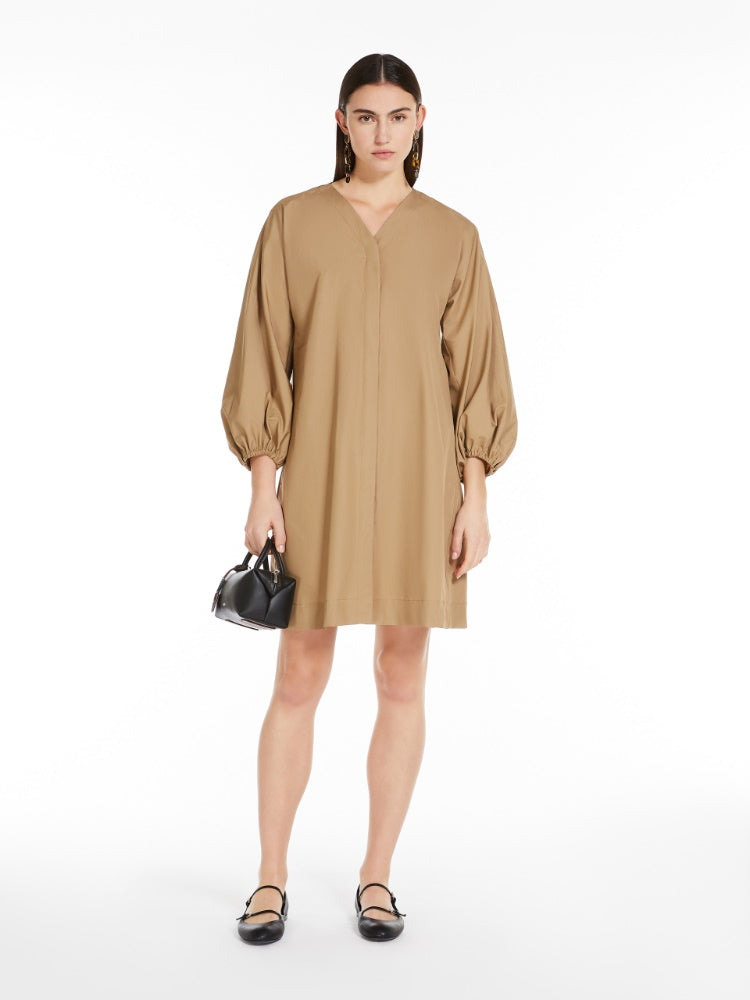 A model wearing a beige short dress with a flared silhouette and slightly puffed three-quarter sleeves with gathering at the cuff, V-neck side inset pockets, and an exquisite lurex jersey intarsia at the back of the neck. The dress has concealed button fastening at the front.