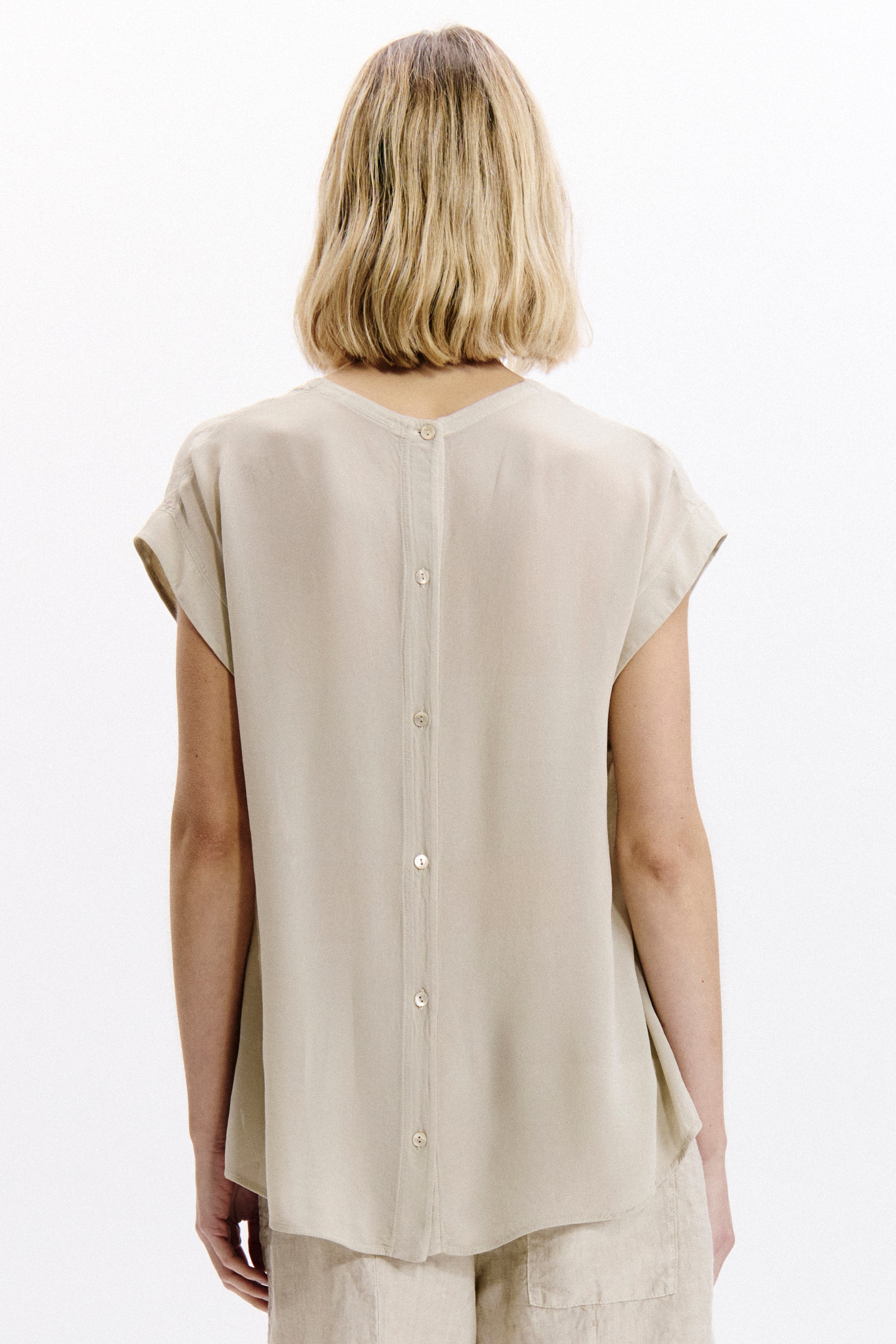 Person wearing a beige sleeveless top on a white background