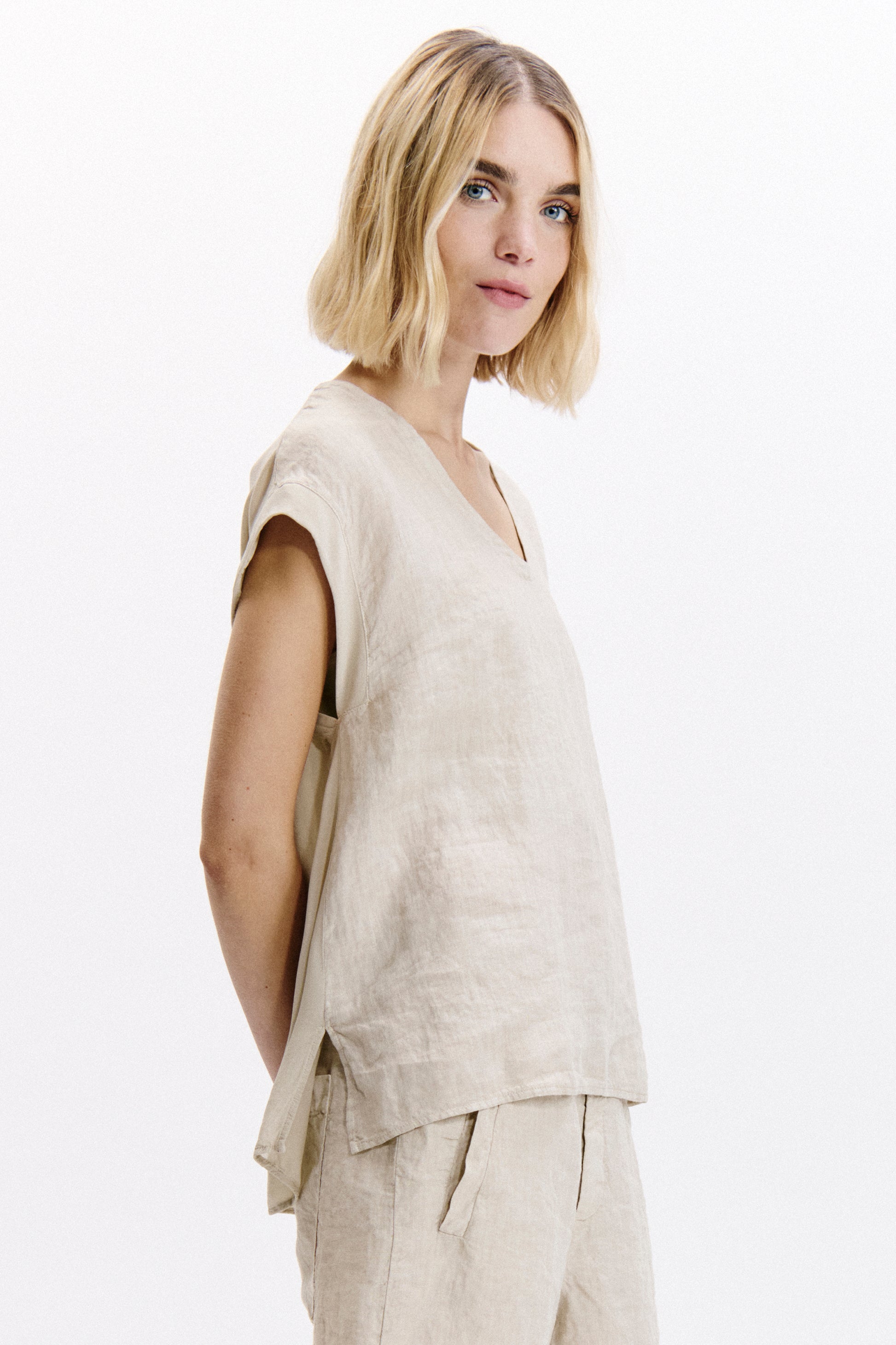 Woman wearing a beige sleeveless top and pants on a white background