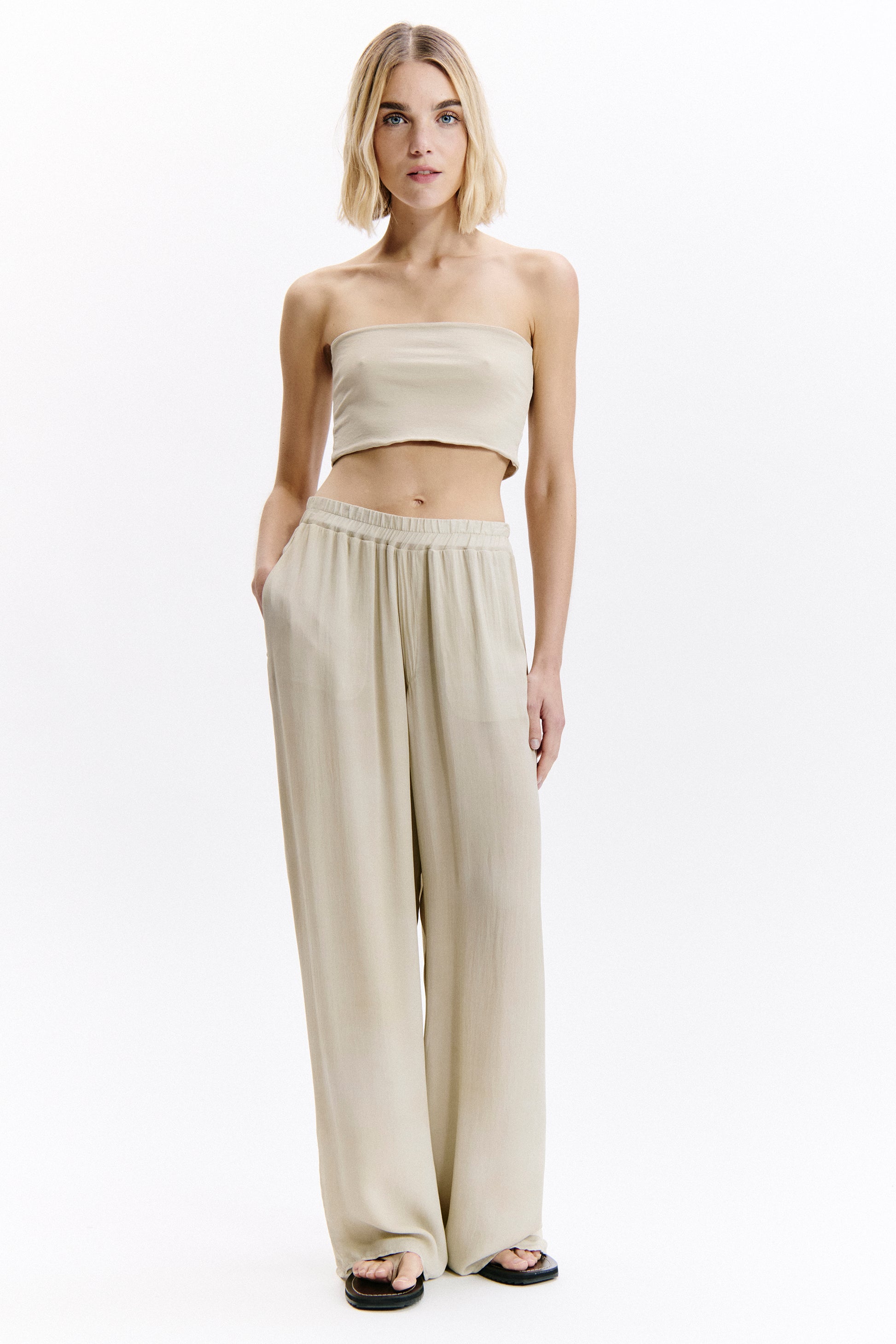 Woman wearing a beige strapless top and wide-leg pants on a white background