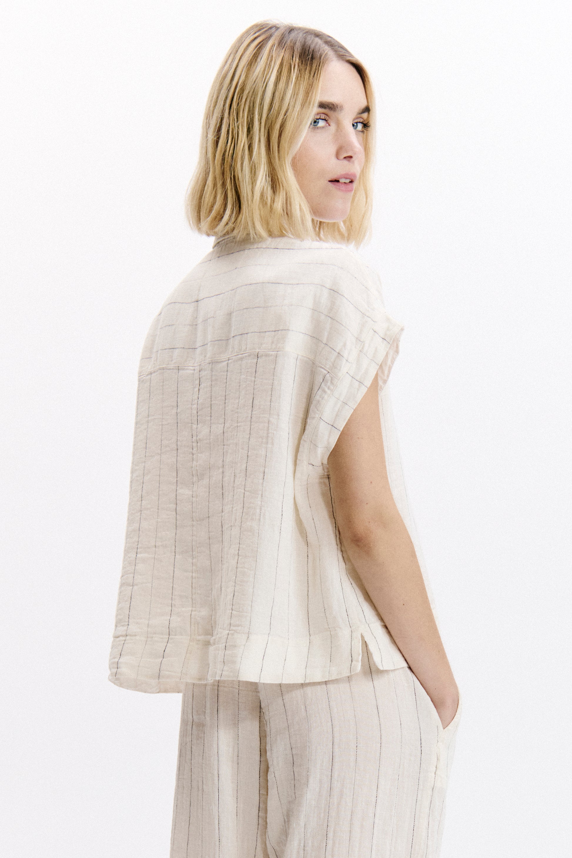 Woman wearing a light-colored sleeveless top and pants on a white background