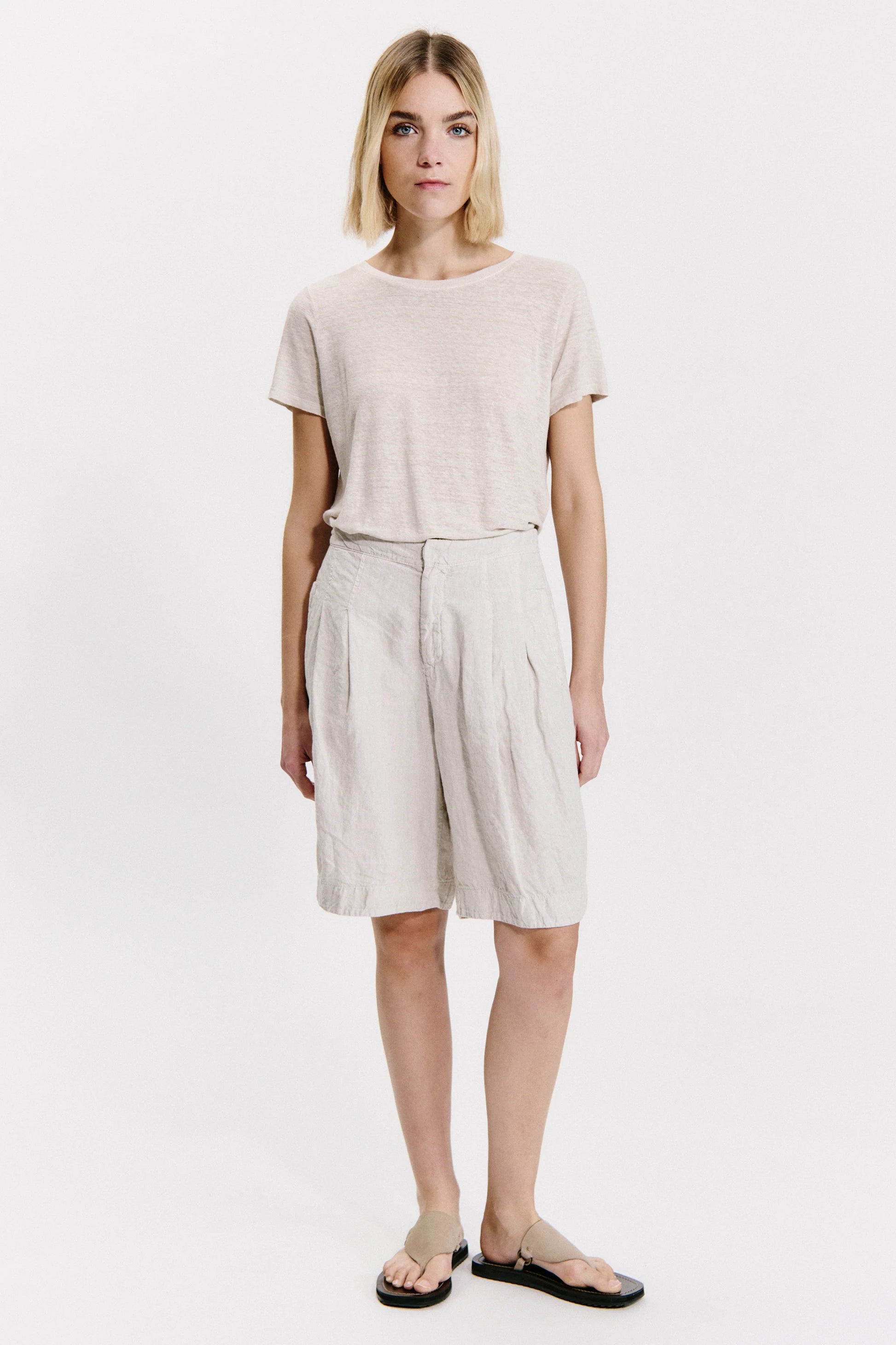 Woman wearing a light pink t-shirt and beige shorts on a white background