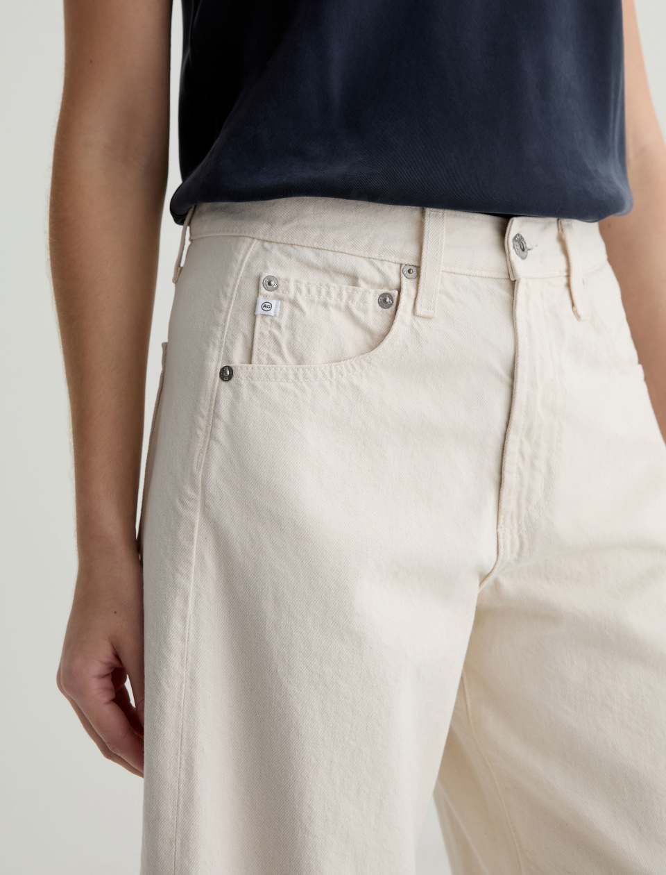 Close-up of a person wearing white jeans and a dark shirt on a plain background