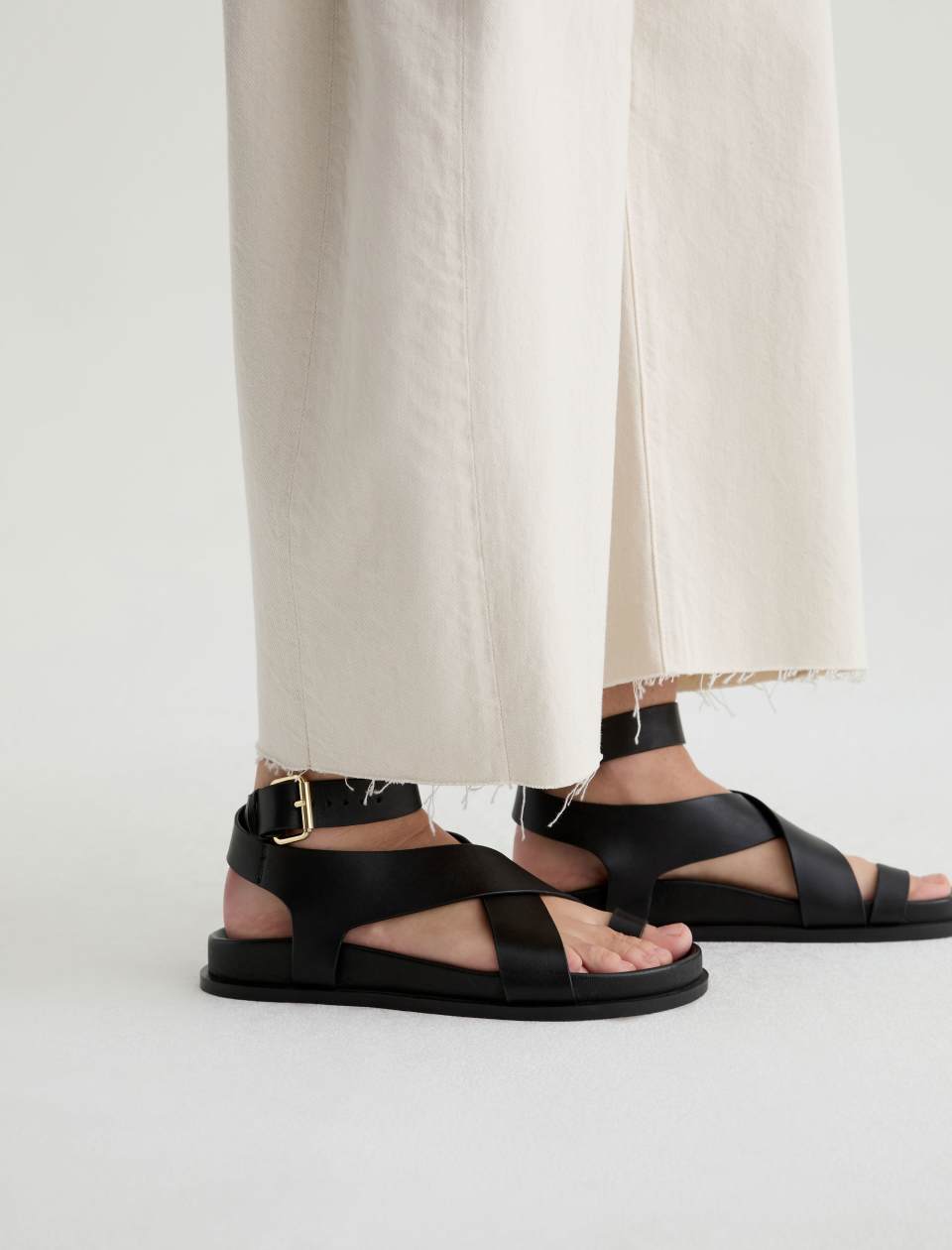 Black sandals worn with beige pants on a white background