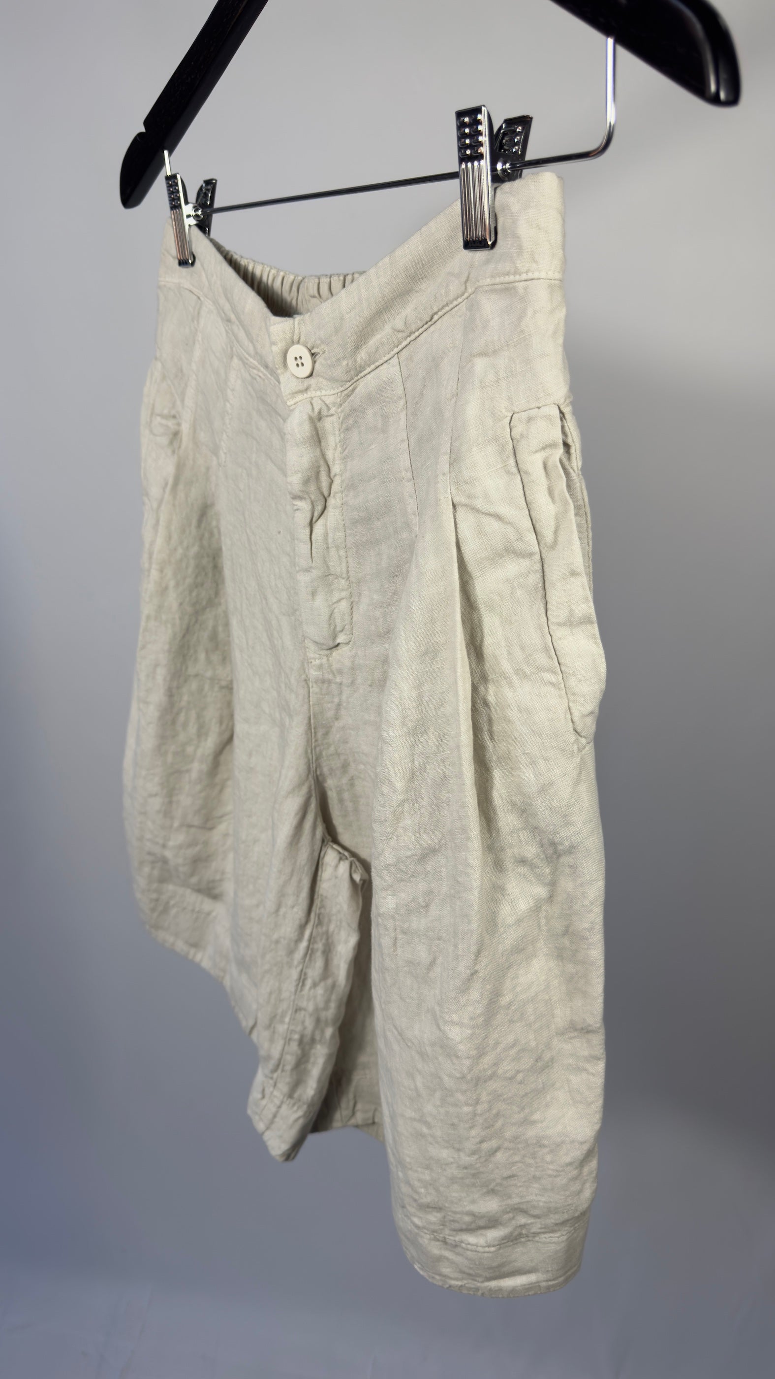 Light-colored pants hanging on a hanger against a gray background