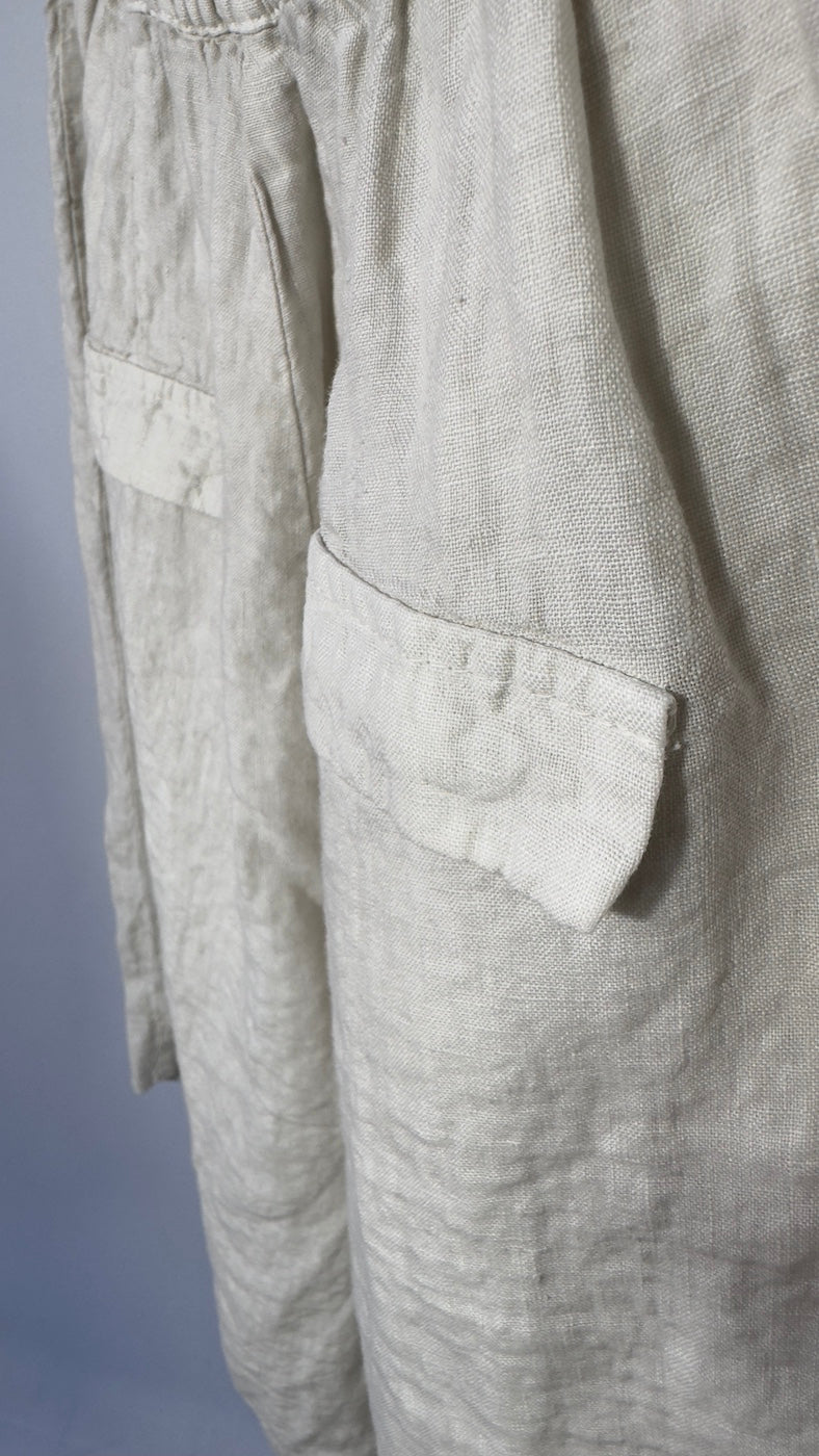 Close-up of light gray pants with a pocket on a plain background