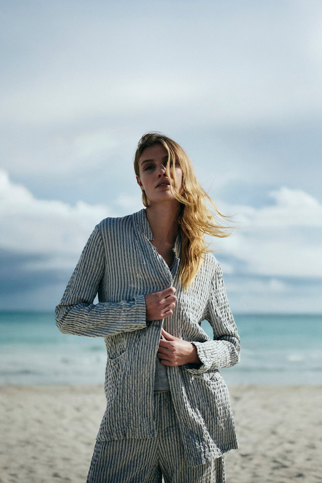 Woman in a striped suit standing on a beach with ocean and sky in the background