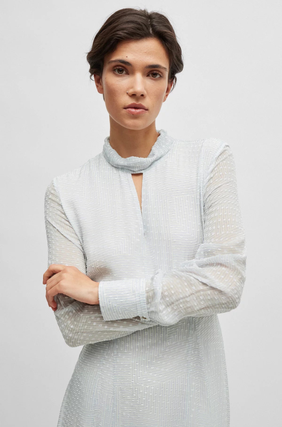 A woman standing with her hands by her sides, wearing a white, V-neck, short-sleeved silk dress with a mid-calf length.