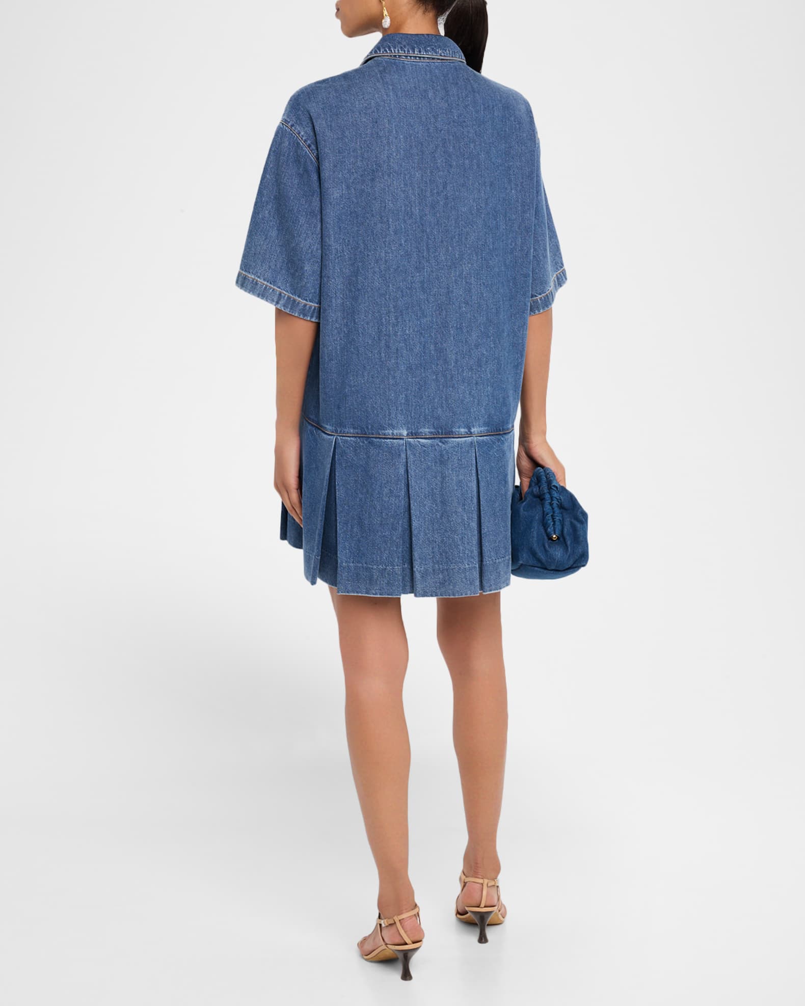 Person wearing a blue denim dress holding a matching handbag on a white background