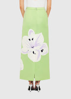 A green skirt with a large floral print in white and purple on the back, worn by a model with a white top and black shoes.