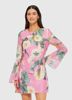 A model wearing a pink mini dress with a floral pattern, long sleeves, and a round neckline.
