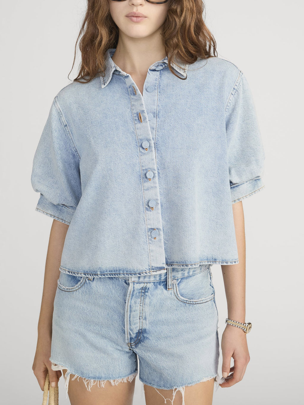 Person wearing a light blue denim shirt and shorts on a white background