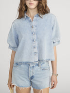Person wearing a light blue denim shirt and shorts on a white background