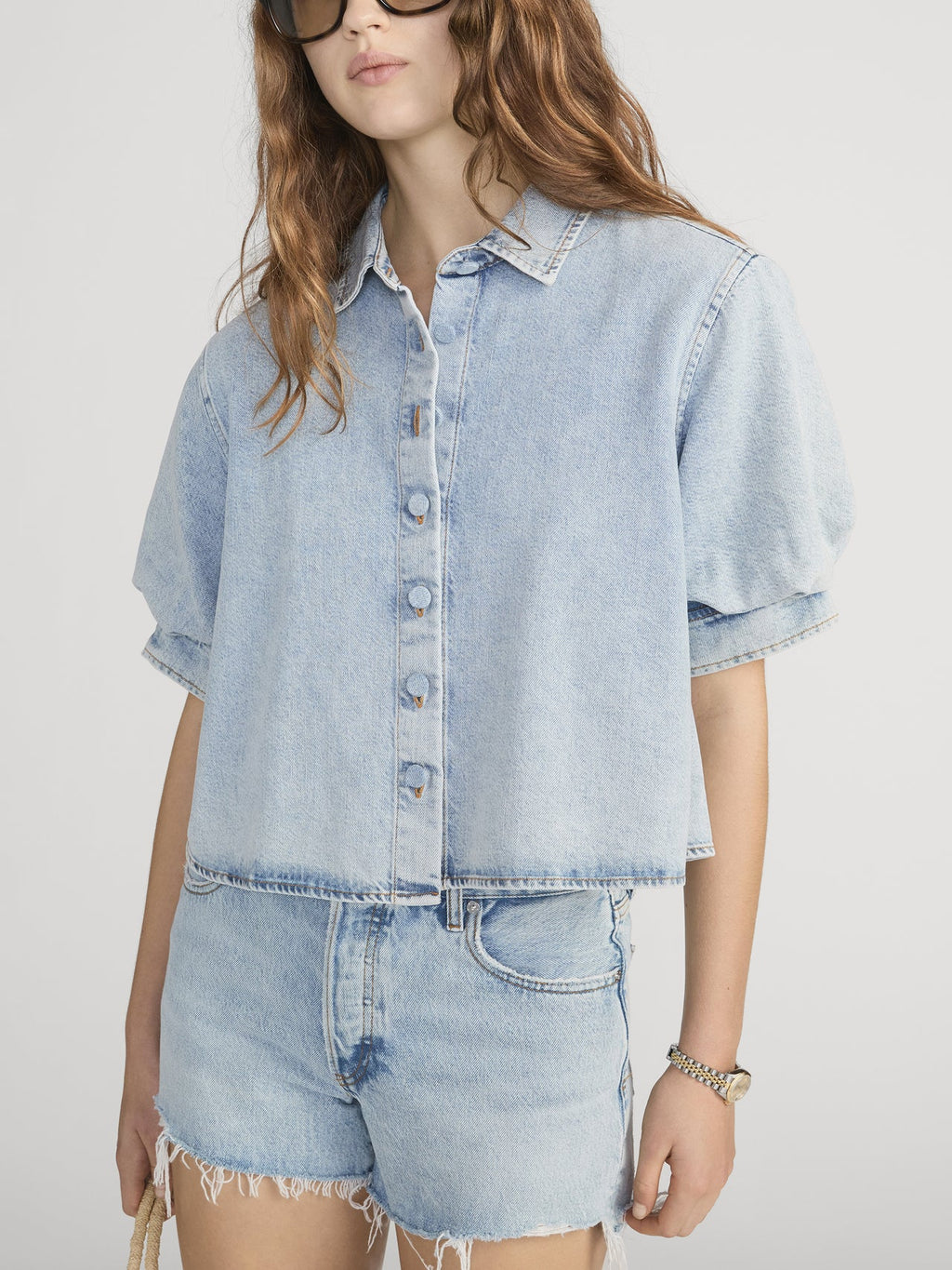 Woman wearing a FRAME BILLOW  light blue denim shirt and shorts on a white background