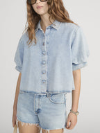 Woman wearing a FRAME BILLOW  light blue denim shirt and shorts on a white background