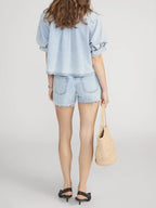 Person wearing a light blue denim outfit with shorts and a bag on a white background