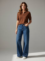 Woman wearing a brown polo shirt and blue jeans against a gray background