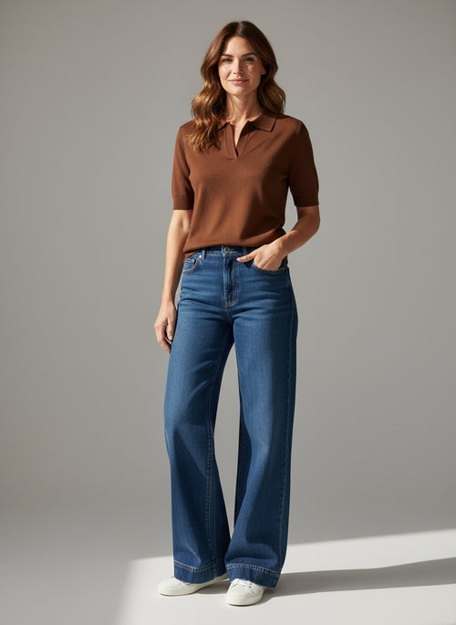 Woman wearing a brown polo shirt and blue jeans against a gray background