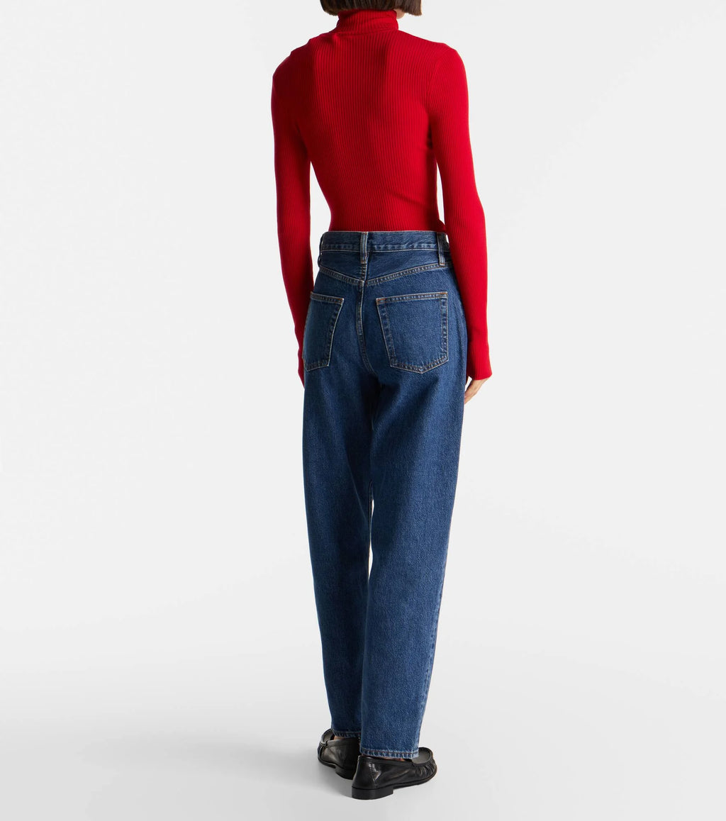 Person wearing a red turtleneck and blue jeans from behind on a white background
