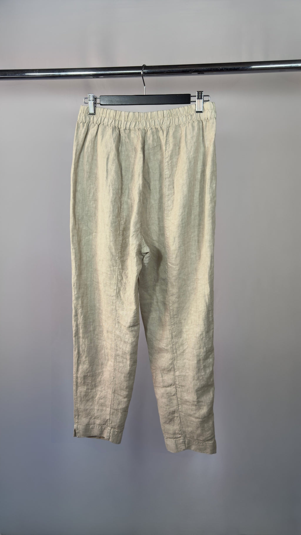Beige pants hanging on a rack against a gray background