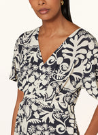 A close-up of a woman wearing a navy and beige floral print dress with short sleeves and a V-neck.