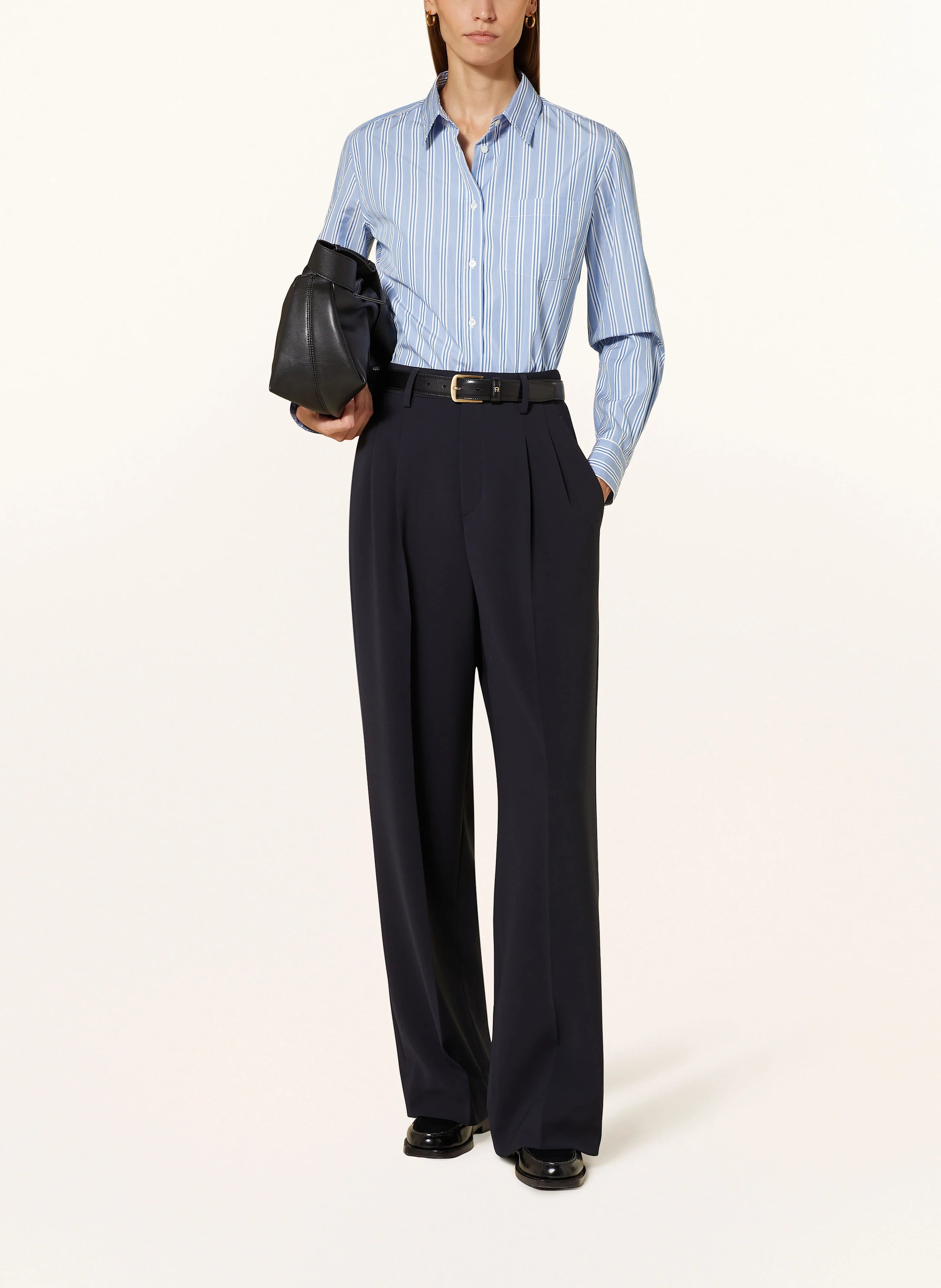 Person wearing a light blue striped shirt and dark pants, holding a black helmet on a white background