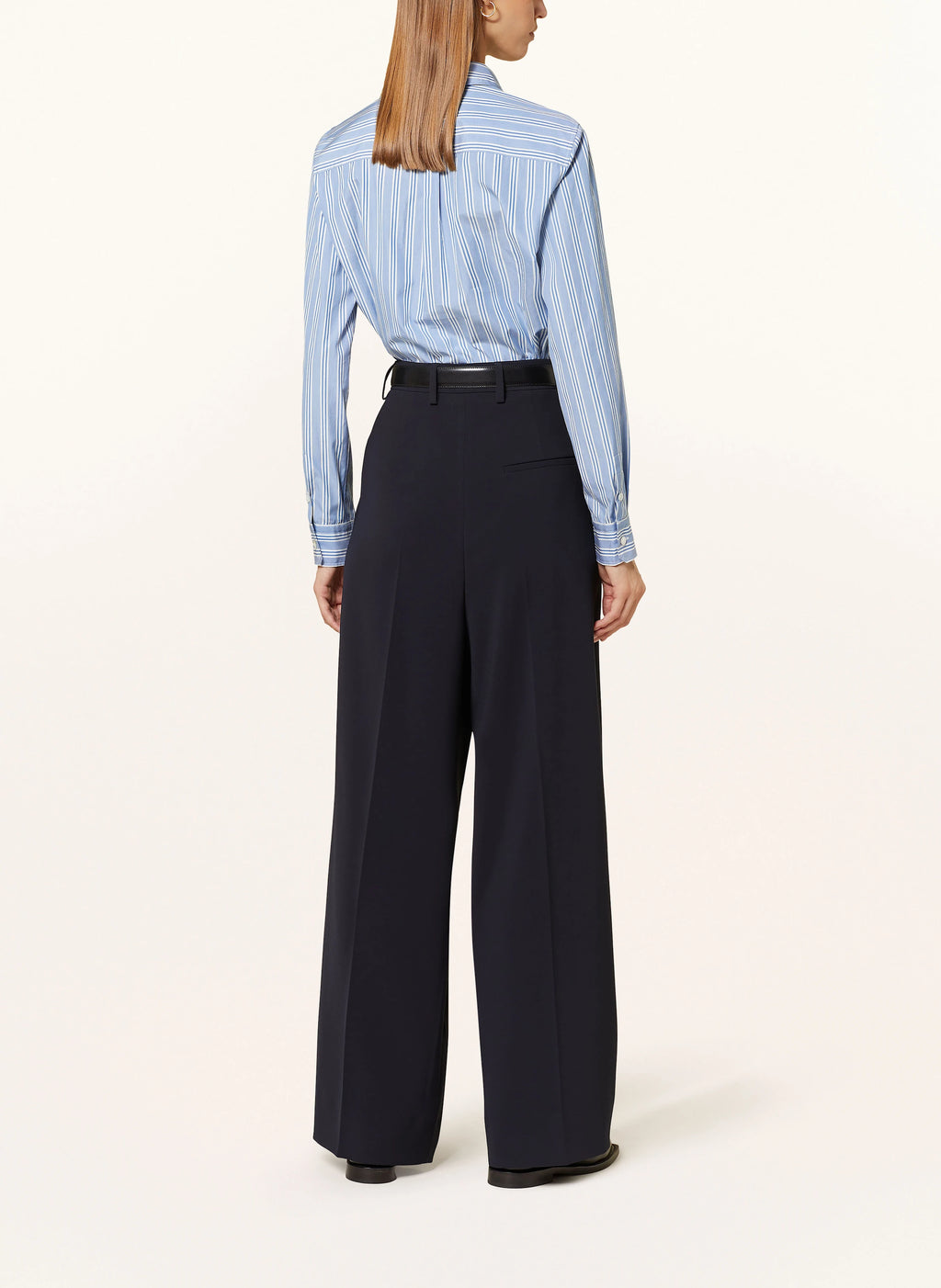 Person wearing a blue striped shirt and black wide-leg pants on a white background