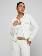 Woman wearing a white denim jacket over a white top and pants on a plain background