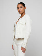 Woman wearing a white denim jacket over a white shirt on a plain background
