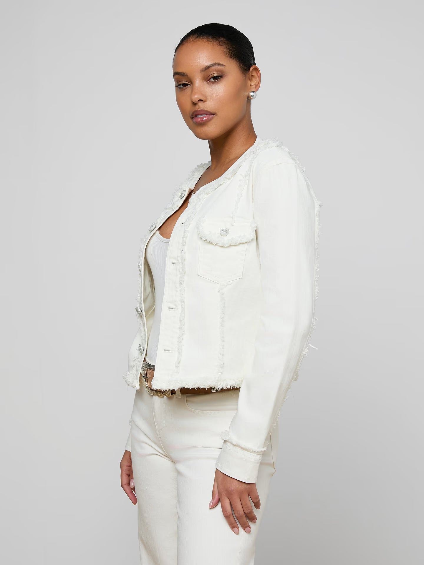 Woman wearing a white denim jacket over a white shirt on a plain background