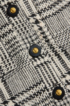 Close-up of a black and off-white woven tweed fabric with a geometric houndstooth-like pattern and decorative round buttons with gold centers.