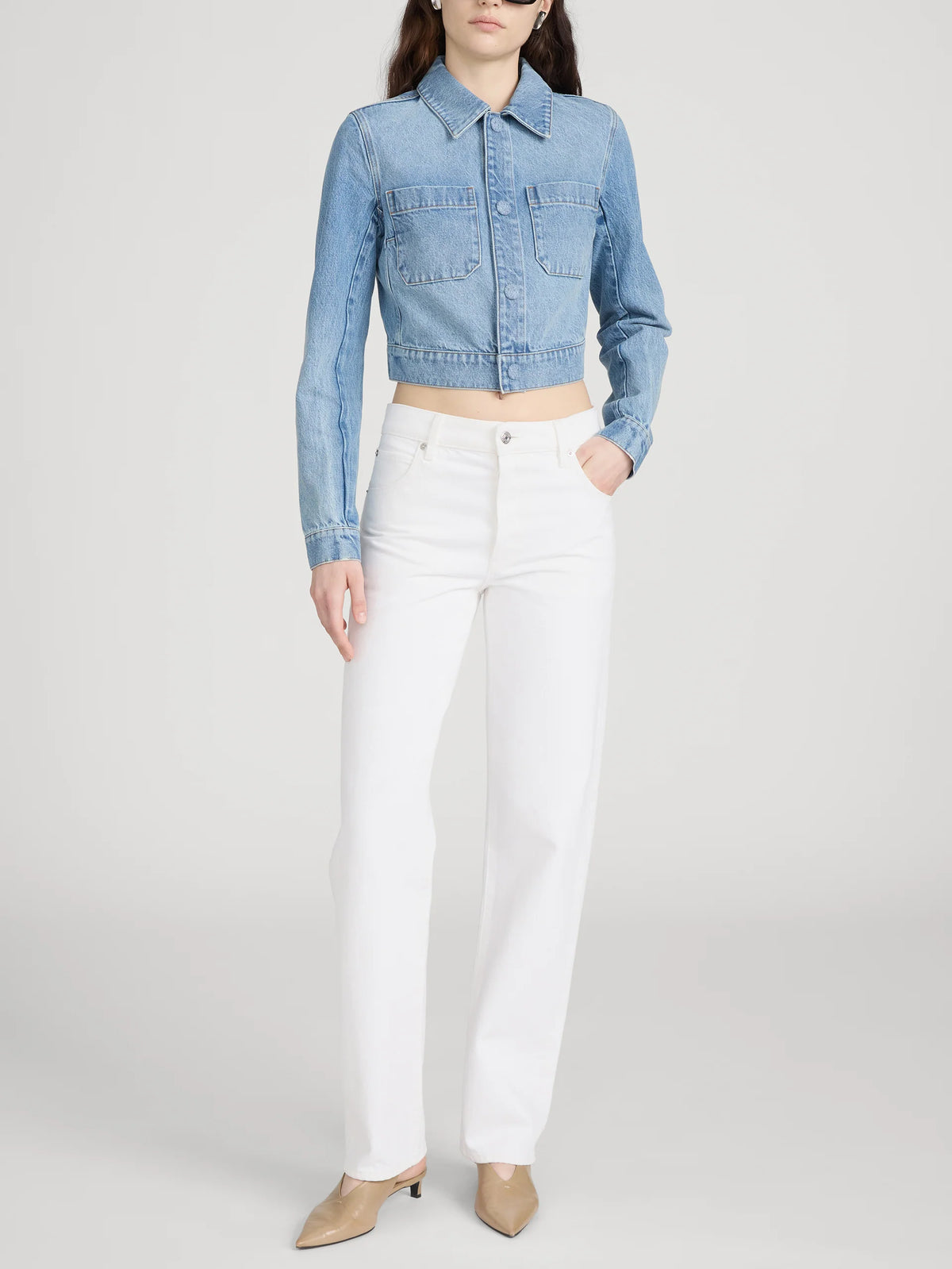 A model wearing a cropped light blue denim jacket and white straight-leg jeans, standing against a light gray studio background.
