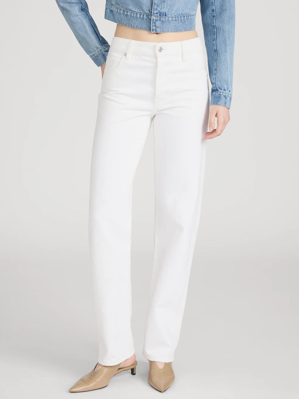 Person wearing white pants and a denim jacket on a plain background