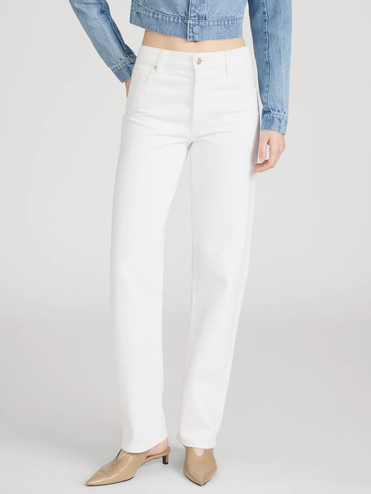 Person wearing white pants and a denim jacket on a plain background