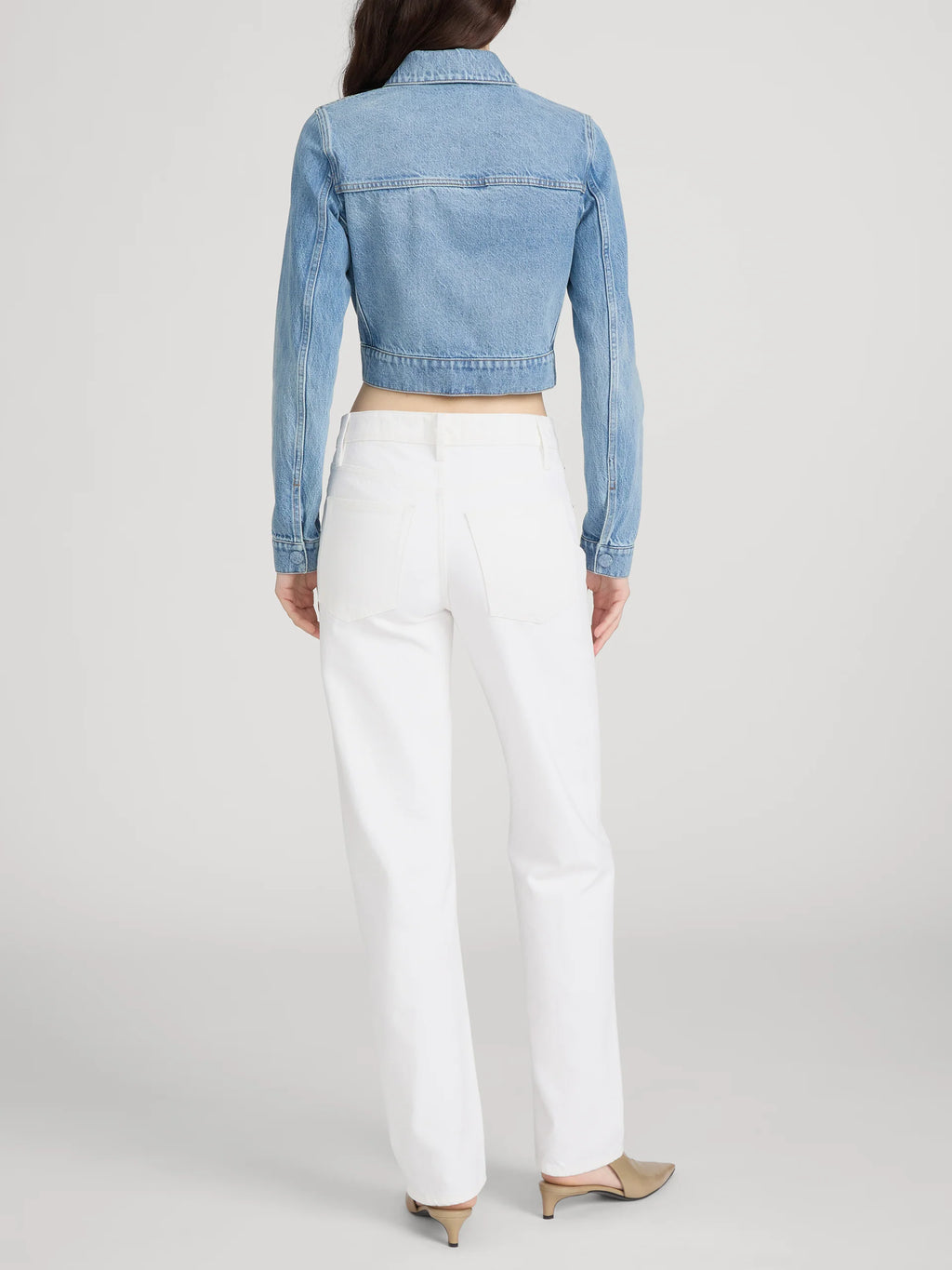 Person wearing a light blue denim jacket and white pants on a plain background