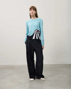 Person wearing a light blue sweater with a black and white design and black pants on a plain background