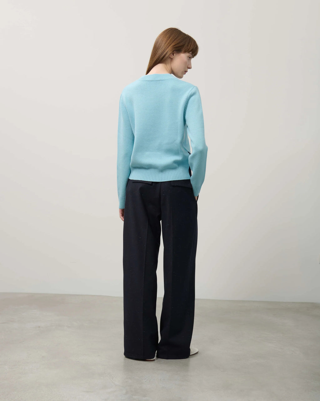 Person wearing a light blue sweater and black pants against a plain background