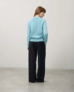 Person wearing a light blue sweater and black pants against a plain background