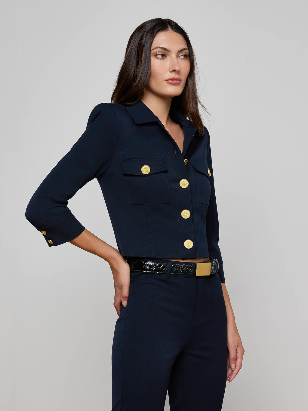 Woman wearing a navy blue jacket with gold buttons on a gray background
