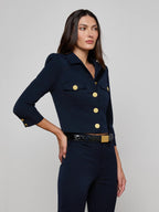 Woman wearing a navy blue jacket with gold buttons on a gray background