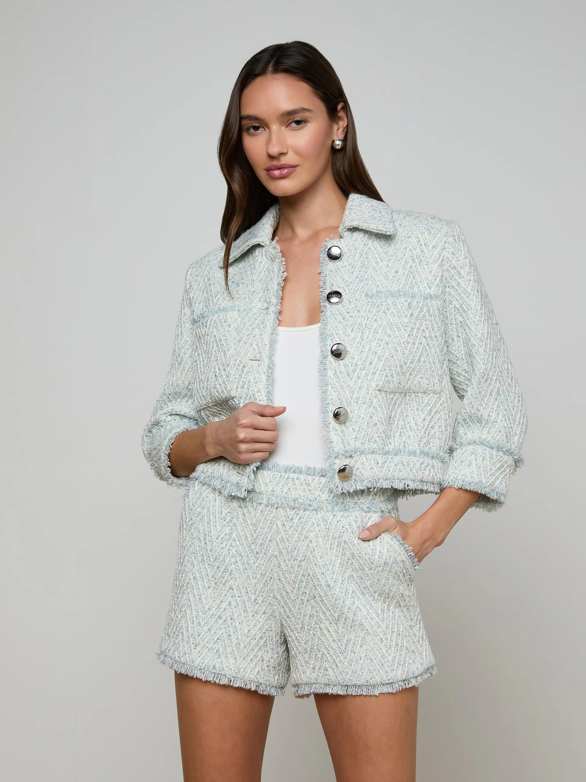 Woman wearing a light gray tweed jacket and shorts set on a plain background