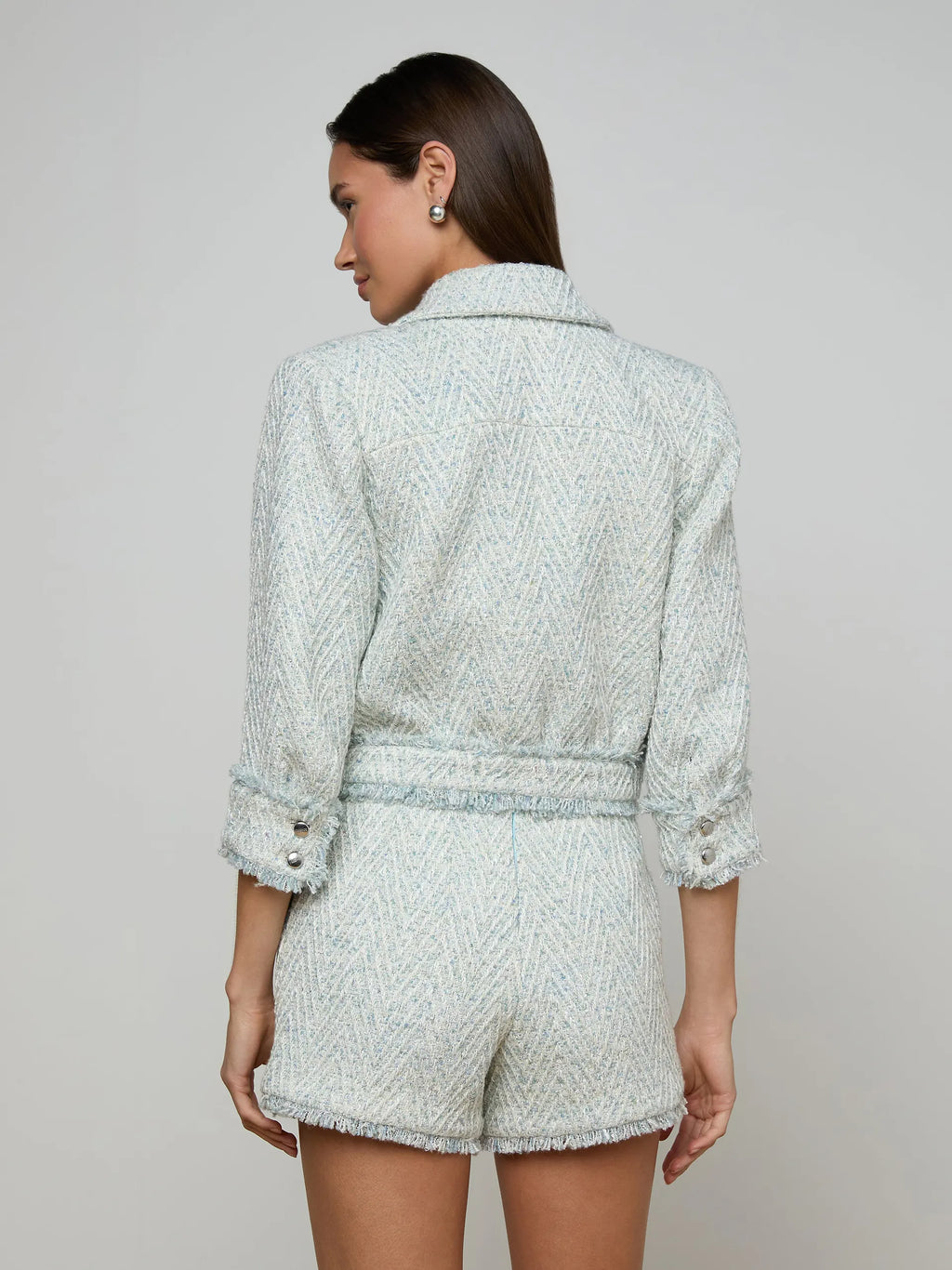 Woman wearing a light gray textured outfit with a matching jacket and shorts on a plain background