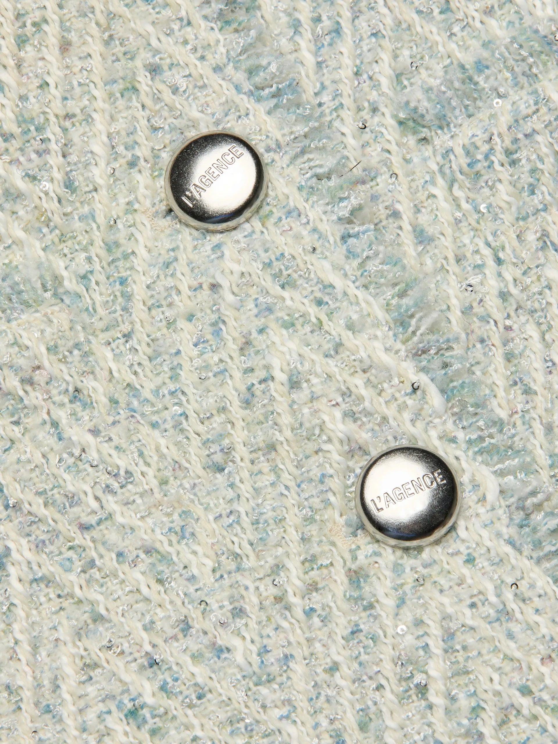 Close-up of a textured fabric surface with two metal buttons labeled 'L'agence'.