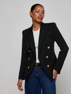 Woman wearing a black blazer with gold buttons on a gray background